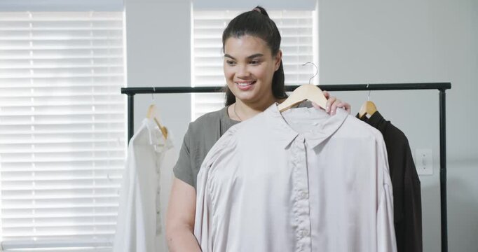African American woman in room choosing blouse on hanger, lifting, pointing collar showing fit