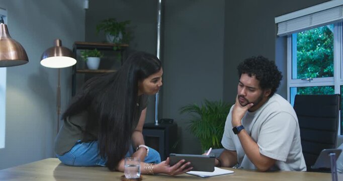 African American couple woman entering frame perching on table holding tablet as man studying notes