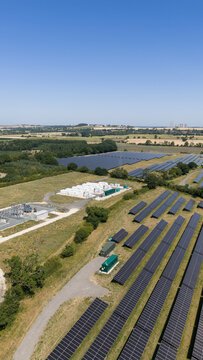 Aerial view of the Tiln Battery Energy Storage System and adjacent solar farm with rows of photovoltaic panels, electrical infrastructure, and green fields in Retford, England, United Kingdom.