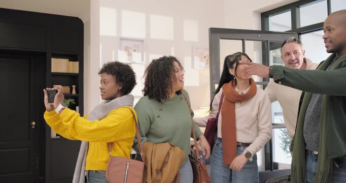 Diverse friends entering home with bags, woman in yellow taking selfies with phone capturing joy