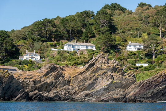 Polperro Cornwall England UK. 11.08.2026. Several white houses are built into a lush green hillside with dramatic rock formations leading down to the sea at Polperro Cornwall.