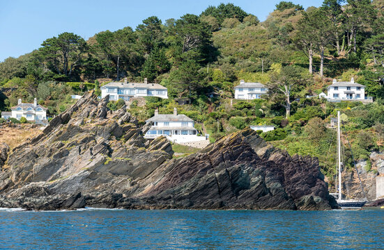 Polperro Cornwall England UK. 11.08.2026. Elegant white houses are built into a lush green slope above a rugged cliff face and blue ocean waters at. Polperro Cornwall.