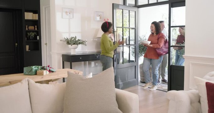 African American woman in headband opening door as holiday guests arriving hugging gifts