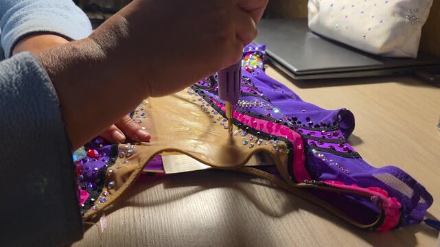 Hand sewing embellishments on a colorful costume with sequins  