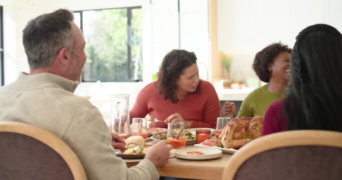 Family sitting around kitchen table, rust sweater woman serving turkey while senior man laughing