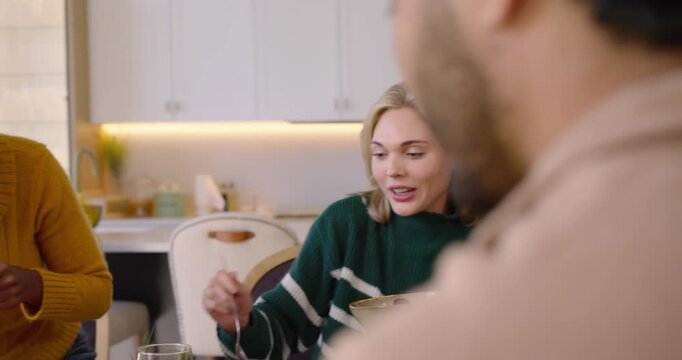 Diverse group sharing meal at dining table, woman in yellow bringing platter, serving turkey