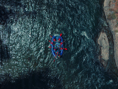 Aerial view of a group of people rafting in a blue boat on the river with rocky banks in Sort, Catalonia, Spain.