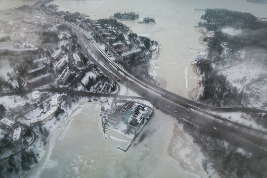 Aerial view of the Herttoniemi district featuring snow-covered buildings, a frozen bay, and highway infrastructure during winter in Helsinki, Uusimaa, Finland.