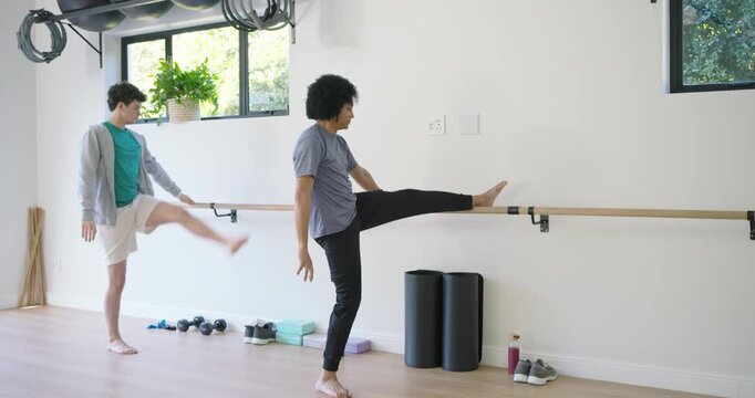 African American men stretching in studio gray tee leader raising arm cueing peer stepping on barre