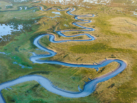 Aerial view of a winding river snaking through the lush green wetlands and grassy plains of the Alaskan tundra in Wasilla, Alaska, United States.