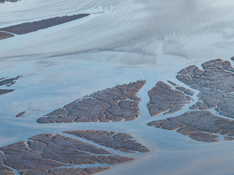 Aerial view of tidal flats and river channels with intricate silt patterns and water flow in the landscape of Wasilla, Alaska, United States.