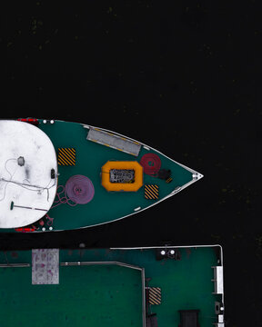 Aerial view of a boat deck with a yellow life raft, coiled ropes, and green flooring floating on dark water in Poland.