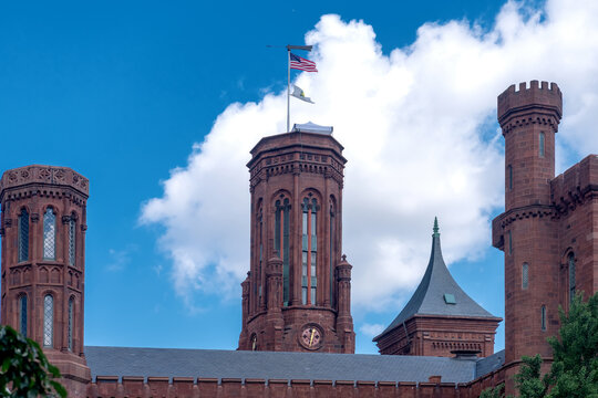 Historic red sandstone Smithsonian Castle rises behind trees in Washington, DC.