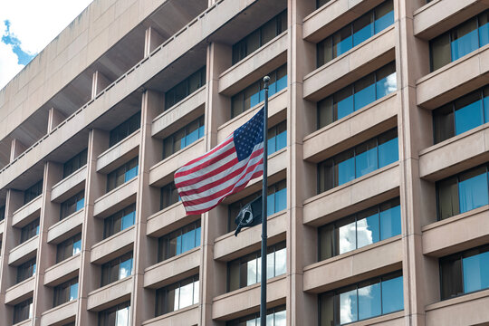 American flag waves before a concrete office building in Washington DC.
