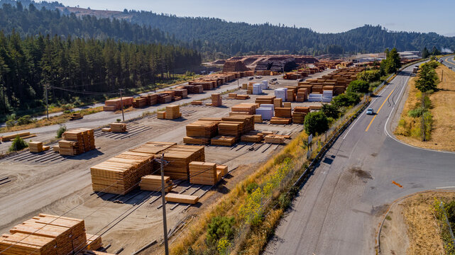 Aerial view of a wood mill with large stacks of lumber and timber arranged in an industrial yard near a forest in Dillard, Oregon, United States.