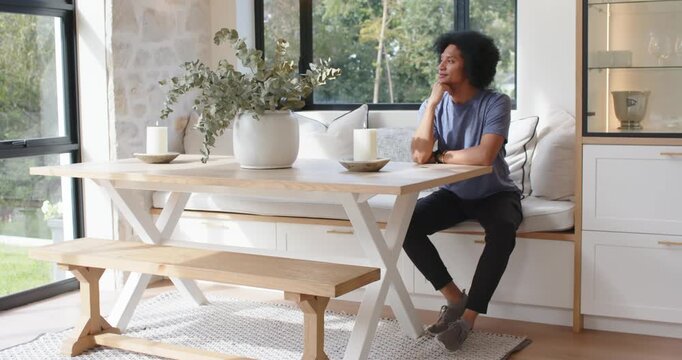 African American man sitting at kitchen table, resting chin, gazing at garden outside, copy space