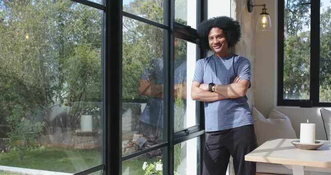 African American man leaning at window at home watching light moving across garden, thinking