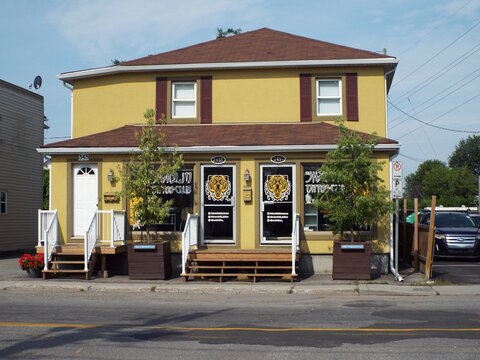 Gatineau, Quebec, Canada &ndash; July 02, 2026: A two-story yellow building features storefront entrances for "Shaolin Tattoo Club" with tiger graphics and wooden entry stairs at 345 Rue Main.