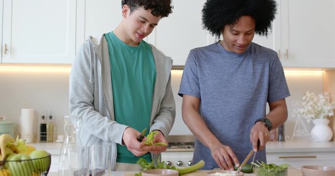 Diverse male friends starting salad prep for lunch, peeling celery and slicing greens on board
