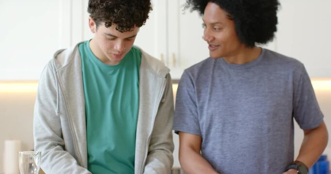 African American male friends teen and man prepping salad at counter, composting scraps in canister