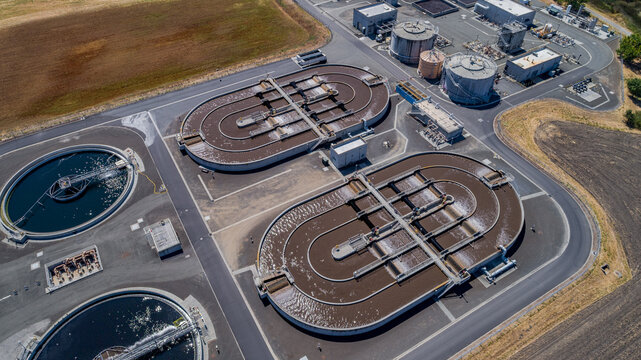 Aerial view of a solar power water treatment plant with large circular and oval sedimentation tanks, industrial infrastructure, and paved roads in Petaluma, California, United States.