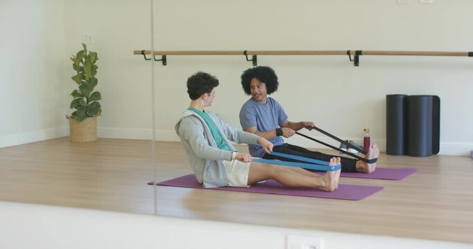African American male trainer cueing male student pulling bands on mats for seated row by mirror