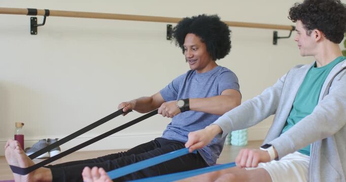Male workout partners pulling resistance bands while counting reps and practicing routine in studio