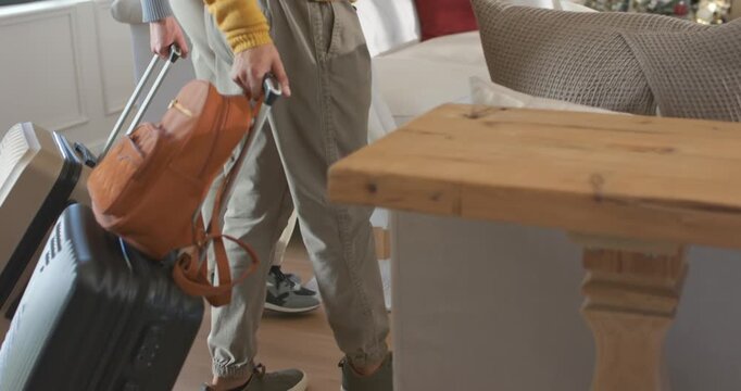 African American men entering home for holiday stay, pulling suitcase and carrying bag, facing tree