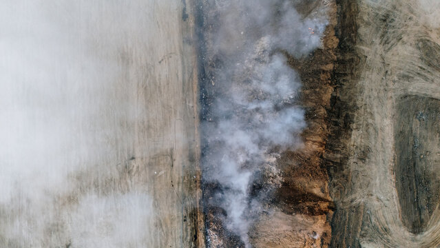 Aerial view of a landfill site with smoke rising from burning waste, surrounded by barren earth and tire tracks in Sremska Mitrovica, Vojvodina, Serbia.