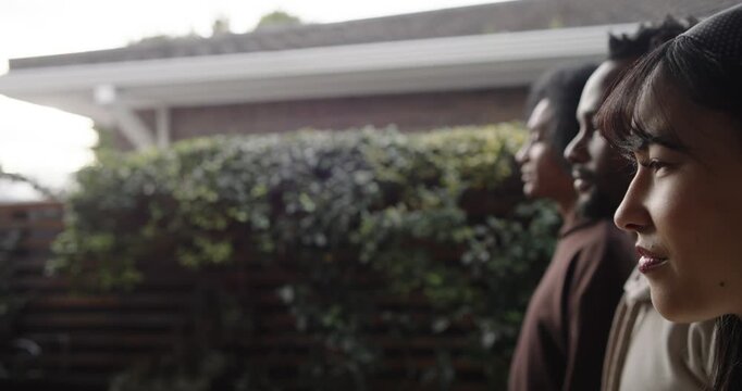 3 friends standing inline by yard hedge in hoodies, camera pulling back revealing faces, copy space