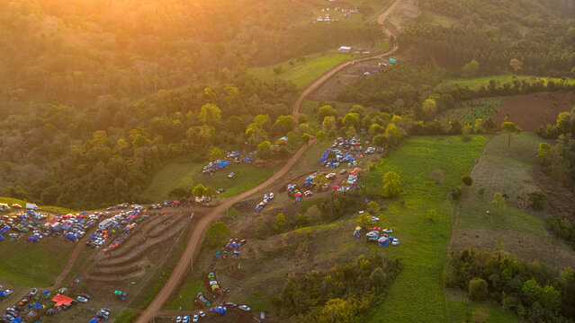 Aerial view of the Rally 2026 Paraguay event with spectators, vehicles, and tents along winding dirt roads in a hilly landscape during golden hour in Nueva Alborada, Itapua Department, Paraguay.
