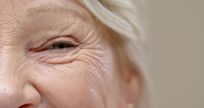 Lady is smiling, left eye narrowing, cheek lifting and wrinkles deepening in studio, copy space