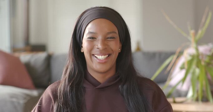African American woman looking at camera, laughing, smiling on couch with headband, engaging viewer