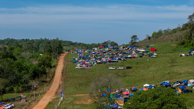 Aerial view of Rally Paraguay 2026 with numerous spectator tents and vehicles parked on a grassy hillside next to a dirt road in Nueva Alborada, Itapua Department, Paraguay.