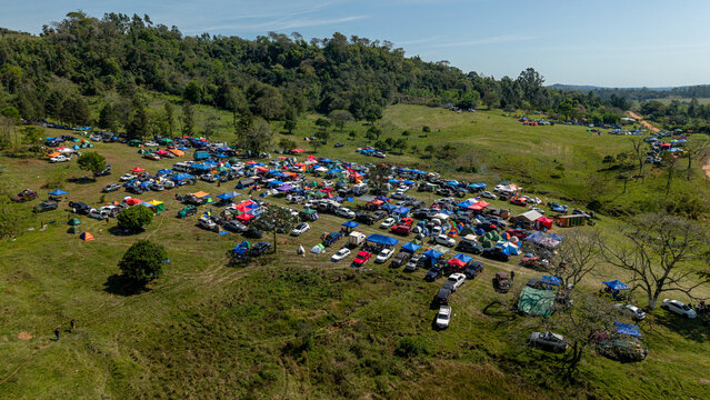 Aerial view of the Rally Paraguay spectator area with numerous parked cars, colorful tents, and crowds gathered on a grassy hillside in Nueva Alborada, Itapua Department, Paraguay.