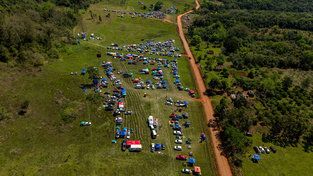 Aerial view of Rally Paraguay 2026 with numerous parked cars and tents scattered across a grassy field next to a dirt road in Nueva Alborada, Itapua Department, Paraguay.