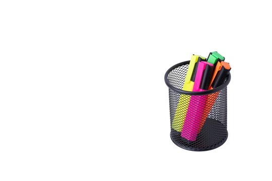 Colorful neon highlighter pens standing in a black wire mesh pen holder on white background