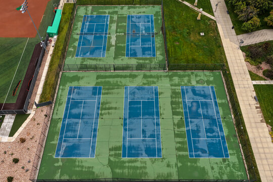 Aerial view of blue and green tennis courts with wet surfaces and cracks in Orem, Utah, United States.