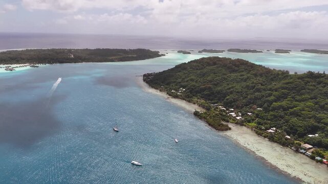 High-altitude aerial drone shot moving forward over Teavanui Pass, showcasing a boat leaving a white wake, anchored sailboats, and the lush coastline of Bora Bora