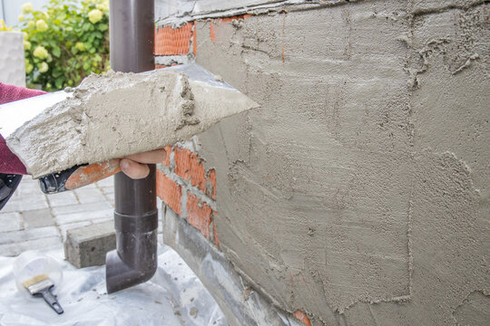 Worker spreads gray mortar on unfinished brick wall
