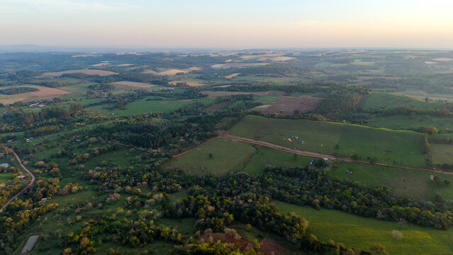 Aerial view of rolling green hills, lush forest patches, and dirt roads winding through the rural landscape of Nueva Alborada, Itapua Department, Paraguay.
