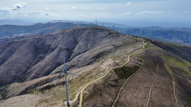 Aerial view of a wind farm with multiple wind turbines situated along a mountainous ridge, featuring dirt access paths and sparse vegetation in Lisbon, Lisbon, Portugal.