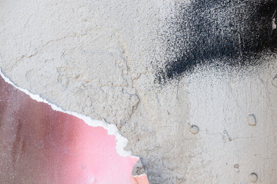 Abstract texture of peeling paint on a wall. The surface shows layers of pink, gray, and black, creating a distressed and weathered appearance.