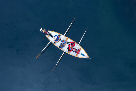 Tighnabruaich, Scotland, United Kingdom - 28 July 2022: Aerial view of Caladh Harbour with a rowing boat carrying people in red and blue jackets on calm dark water.