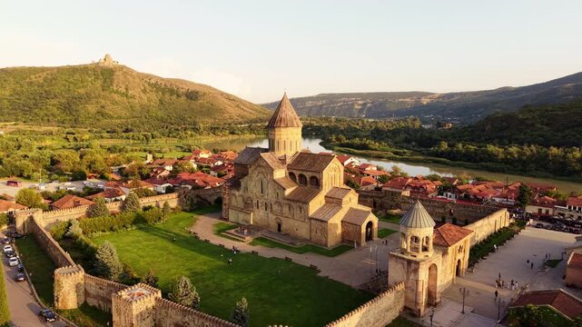Spiritual aerial view of Svetitskhoveli Cathedral at sunset in Mtskheta, Georgia, with Jvari Monastery and the Mtkvari River creating a sacred historic landscape.
