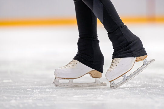 young figure skater's legs in white skates glide across the rink. A close-up of a woman's legs in skates on the ice. Conceptual representation of winter sports, training, and an active lifestyle.