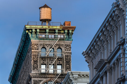 UNITED STATES, NEW YORK CITY, MANHATTAN, SOHO. THE SILK EXCHANGE BUILDING WITH TERRA COTTA ORNAMENTATION, COPPER CORNICE, PAINTED IRON FIRE ESCAPE AND WATER TOWER LIT BY SYNSET LIGHT