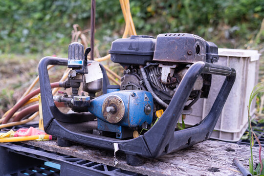 Engine powered agricultural sprayer with pump and hose set up beside a farm field