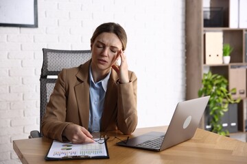 Fototapeta premium Stressed businesswoman in suit with glasses near laptop at desk in office