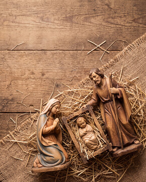 Overhead flat lay of a wooden nativity scene with baby Jesus, Mary, and Joseph on straw and rustic wood background